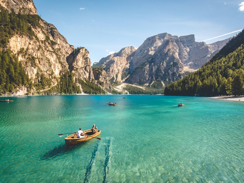 The rowboat seen wide — tiny on a huge turquoise lake, with cliffs and mountains all around it.