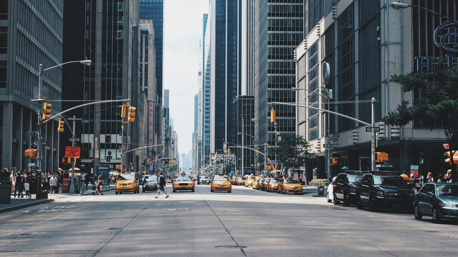 The same city street one second later — sharp, with a single person caught mid-stride crossing between yellow cabs.